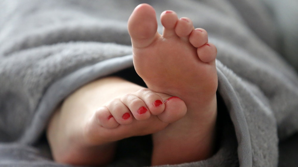Eine Frau schläft in einem Bett und streckt die Füße unter der Decke hervor.
