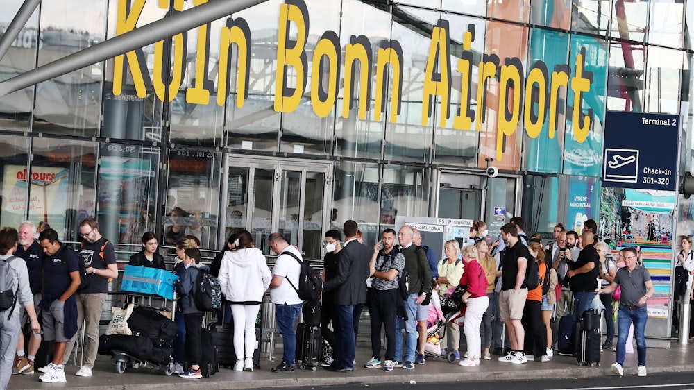 Fluggäste warten am Flughafen Köln/Bonn in einer Reihe.