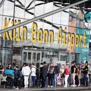 Fluggäste stehen am Flughafen Köln/Bonn in der Warteschlange, die bis vor das Terminal reicht.