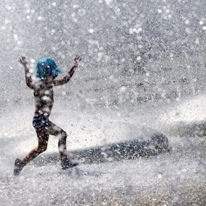 Ein Kind spielt in einem Brunnen in München im Wasser.