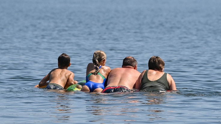 Eine Familie schwimmt auf einer Luftmatratze im Wasser des Storkower Sees.