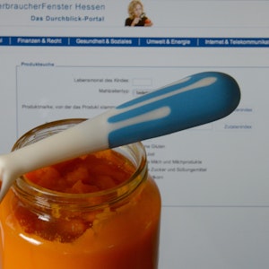 Ein Glas mit Karottenbrei für Babys steht vor einem Laptop-Monitor mit der geöffneten Seite einer Online-Datenbank zur Babynahrungs-Produktsuche.