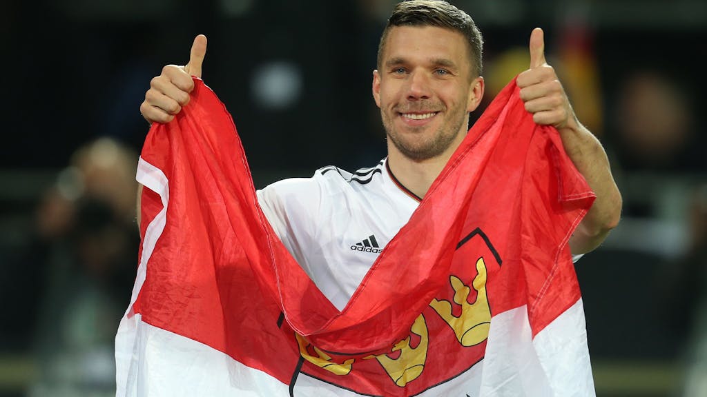 Lukas Podolski aus Deutschland verabschiedet sich nach dem Spiel von den Fans und hält dabei eine Kölner Fahne.