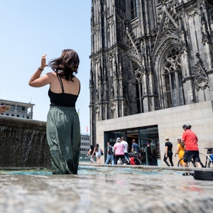 Zwei Frauen erfrischen sich in einem Brunnen am Kölner Dom. Bald rollt die nächste Hitzewelle auf Köln zu.