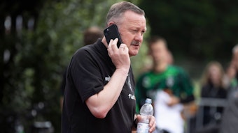 Sportdirektor Roland Virkus von Borussia Mönchengladbach am 8. Juli 2022 im Rahmen des Trainingslagers in Rottach-Egern. Virkus hält sich mit der rechten Hand ein Smartphone ans Ohr und telefoniert, in der linken Hand hält er eine Wasserflasche.