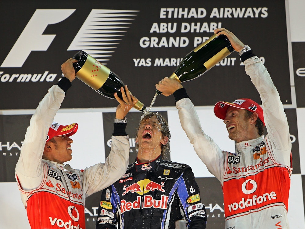 Lewis Hamilton (l.) und Jenson Button (r.) überschütten Vettel mit Champagner.
