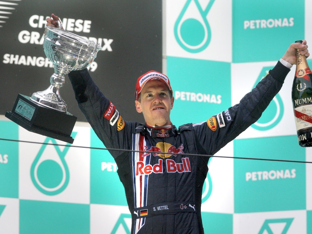 Sebastian Vettel beim Rennen in China auf dem Podium – zu seiner rechten der Pokal und in seiner linken Hand eine Champagnerflasche.
