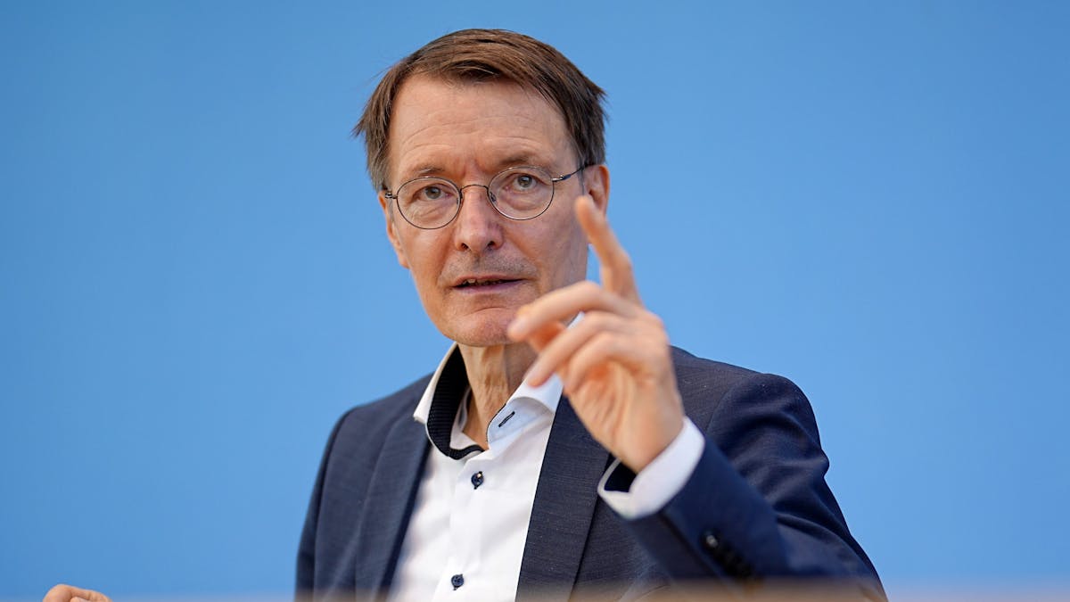 Bundesgesundheitsminister Karl Lauterbach hebt vor einer blauen Wand mahnend den Zeigefinger