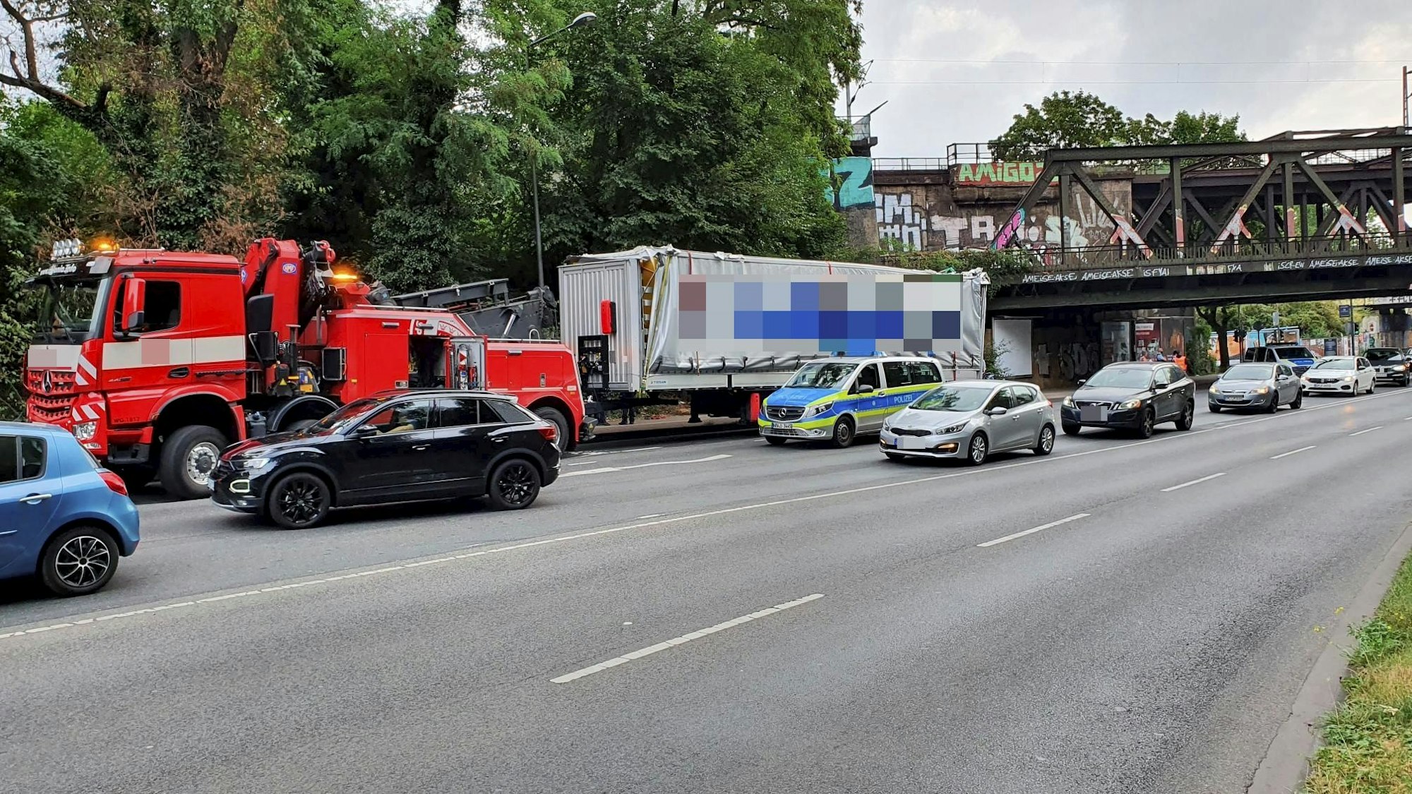Ein beschädigter Lkw-Anhänger steht ein paar Meter hinter einer Eisenbahnbrücke, neben dem Anhänger steht ein Polizeifahrzeug.