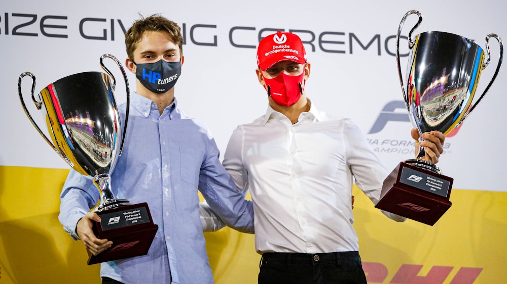 Oscar Piastri und Mick Schumacher tragen beide jeweils einen Pokal und blicken in die Kamera.