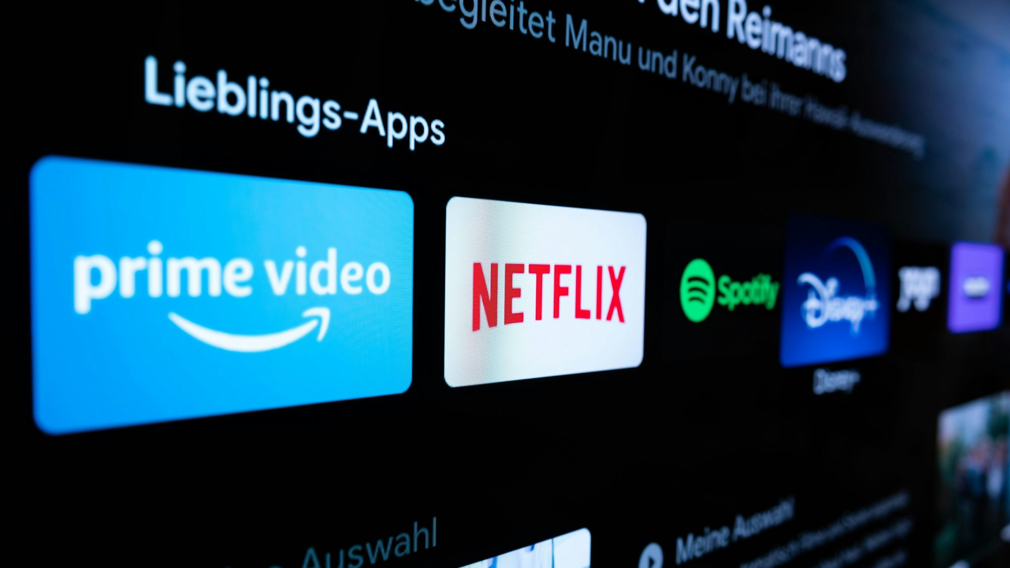 Auf einem Fernseher in einer Wohnung sind verschiedene Streaming-Dienste, darunter Amazon Prime Video (l-r), Netflix, Spotify und Disney+ zu sehen.