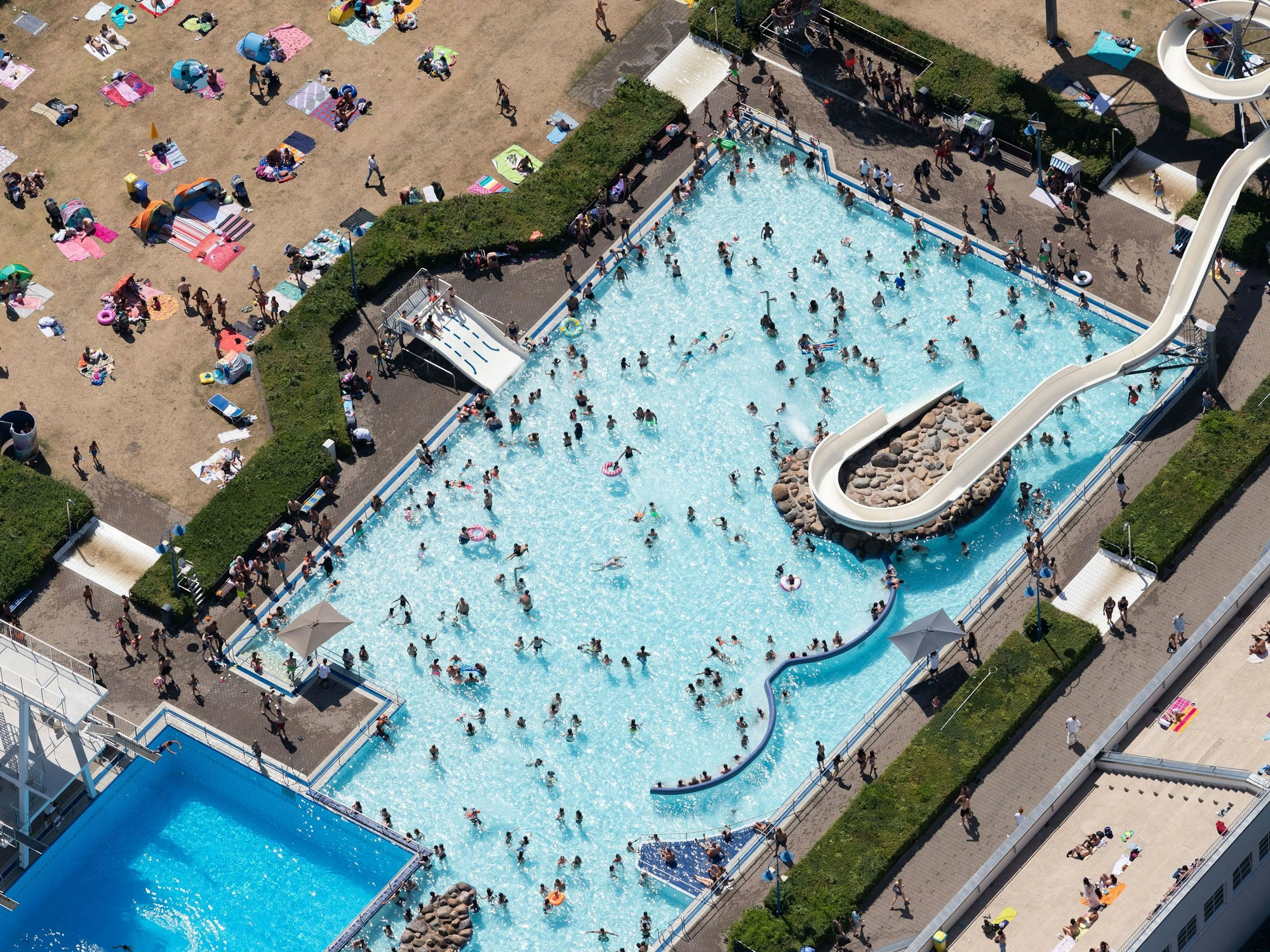 Luftaufnahme eines Freibads mit diversen Besucherinnen und Besuchern.