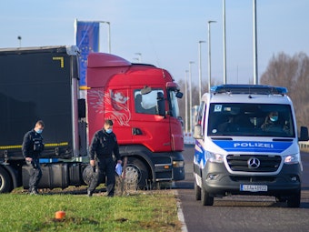 Polizisten gehen zu ihrem Fahrzeug während dahinter ein Lastwagen seinen Stellplatz verlässt.
