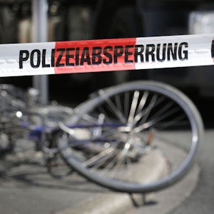 Demoliertes Fahrrad liegt auf einer Straße, davor ein Absperrband der Polizei.