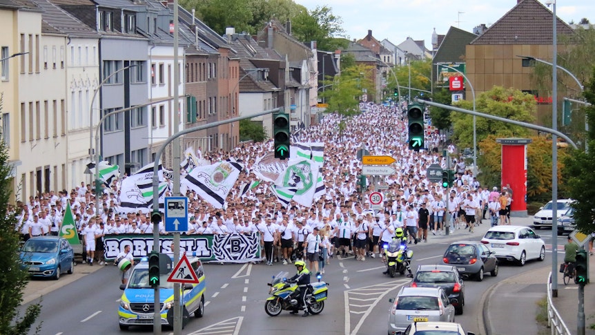 Tausende Menschen haben am Marsch der Fans von Borussia Mönchengladbach vor dem Bundesliga-Heimspiel am 6. August 2022 gegen die TSG Hoffenheim teilgenommen. Zu sehen sind Fahnen und Fans, die weiße Trikots oder T-Shirts tragen.