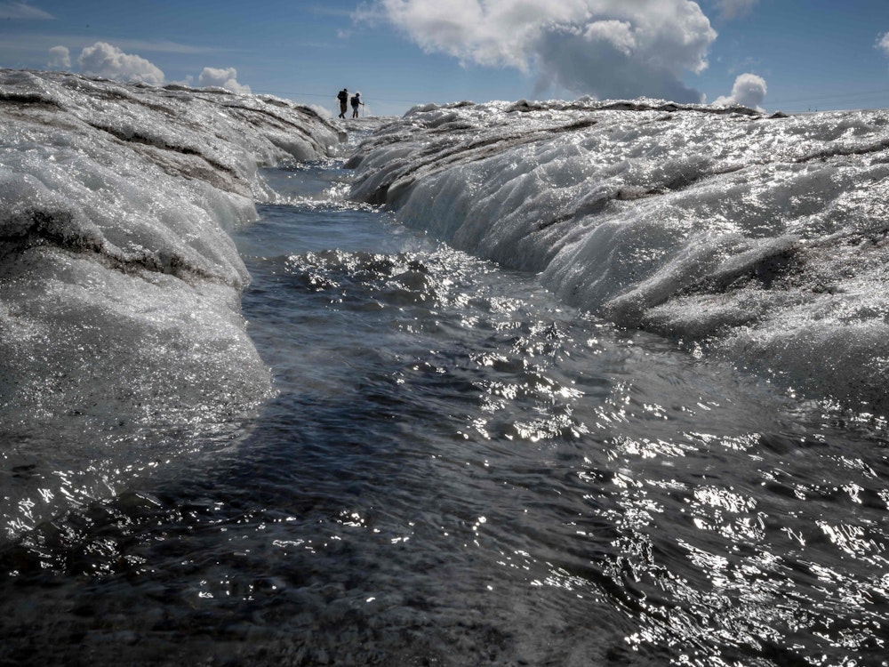 TOPSHOT - A picture taken on August 6, 2022 shows tourists walking next to a meltwater stream flowing from the Tsanfleuron Glacier above Les Diablerets, Switzerland. - Following several heatwaves blamed by scientists on climate change, Switzerland is seeing its alpine glaciers melting at an increasingly rapid rate. (Photo by Fabrice COFFRINI / AFP)