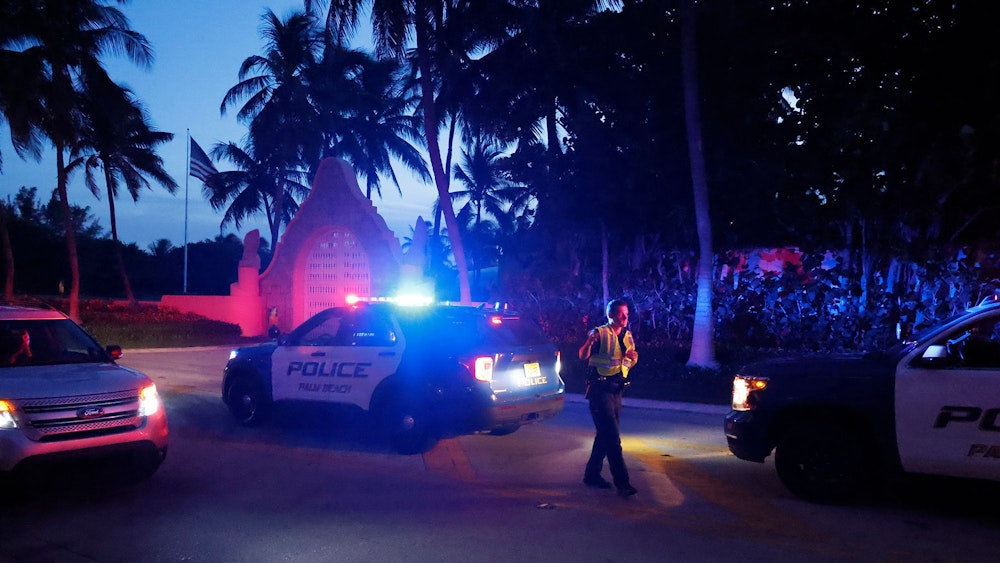 Das undatierte Symbolfoto zeigt drei US-amerikanische Polizeiwagen mit Blaulicht und einen uniformierten Polizisten vor einem Tor. Überall stehen Palmen.