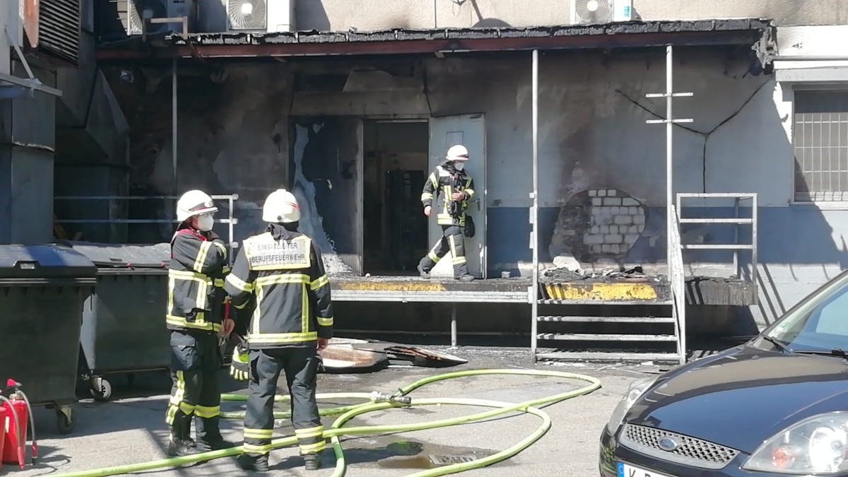 Ein Feuerwehrmann kommt aus einem Gebäude, in dem es gebrannt hat, zwei Kollegen stehen davor, zu ihren Füßen Löschschläuche.&nbsp;