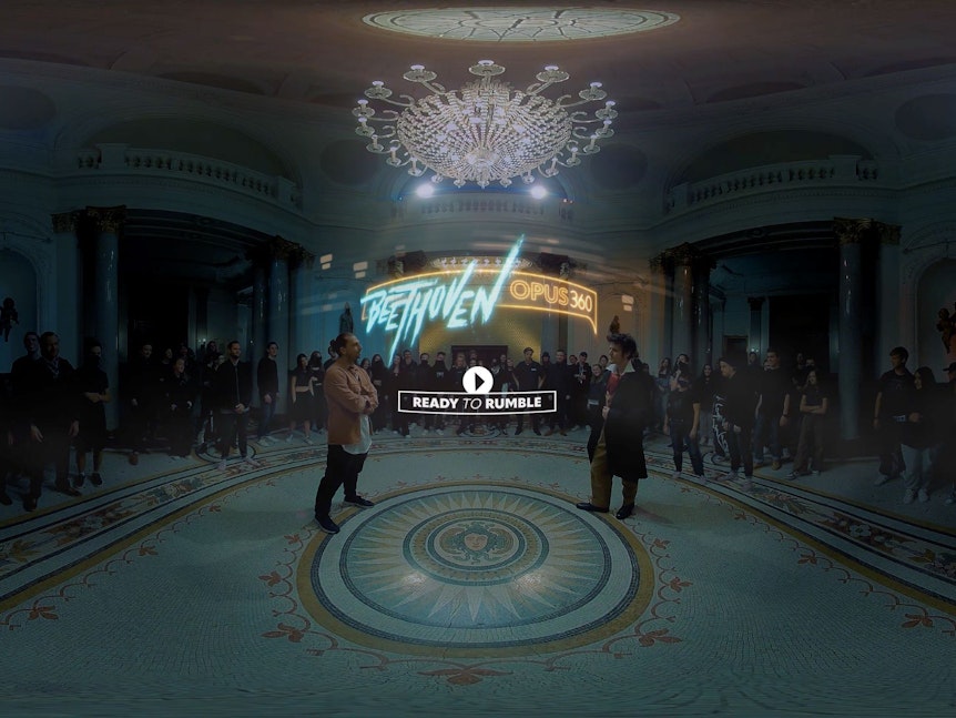 Ein Screenshot aus dem VR-Spiel zeigt Beethoven und einen Rapper, die sich in einem barocken Saal umgeben von Menschen gegenüber stehen.