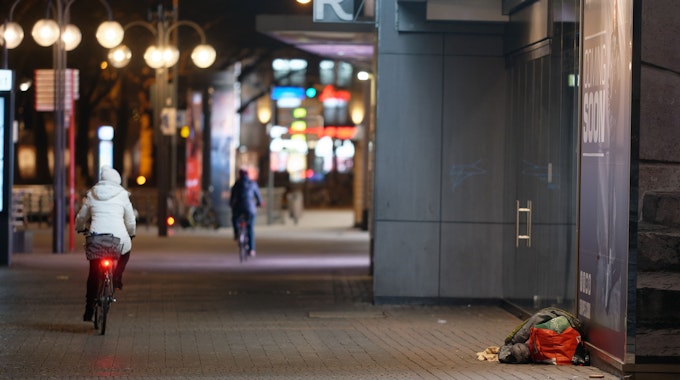 Ein Mensch liegt in der Innenstadt in einem Schlafsack im Eingang zu einem Geschäft.