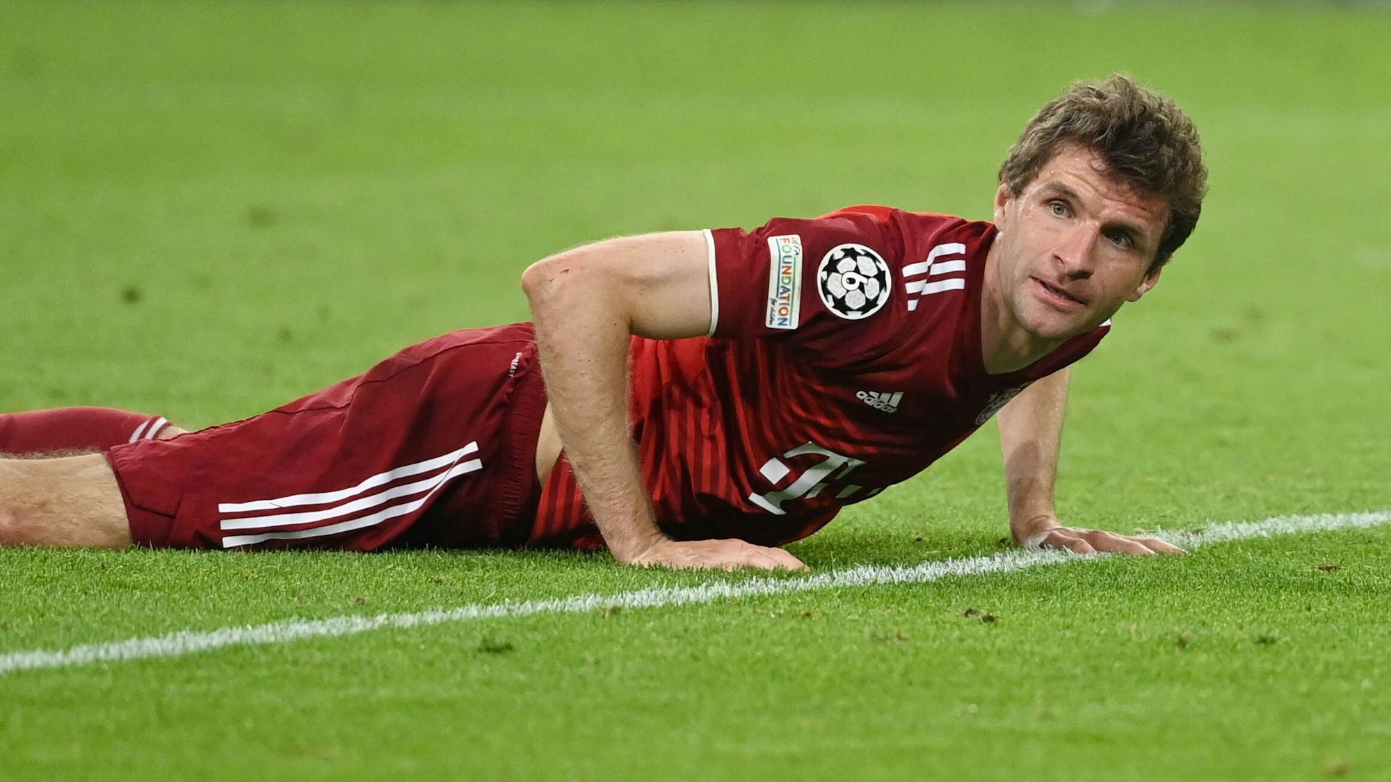 Thomas Müller stützt sich mit beiden Händen auf dem Rasen ab.