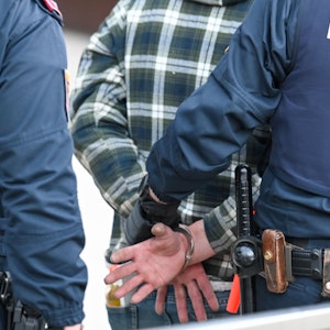 Zwei Polizeibeamte führen einen Mann in Handschellen ab.
