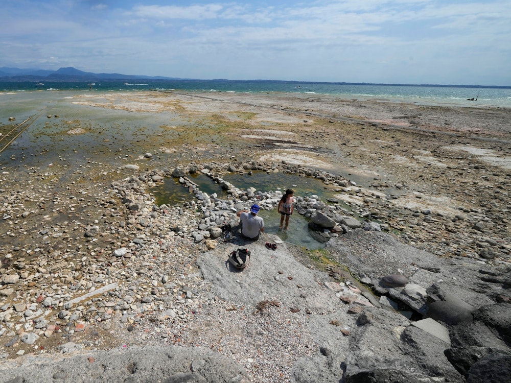 Freitag, 12. August: Ein Mann sitzt neben einem Kind am Gardasee. Der Wasserstand des Gardasees ist nach einer schweren Dürre stark gesunken, wodurch die Steine, die die Halbinsel von Sirmione umgeben, freigelegt wurden.