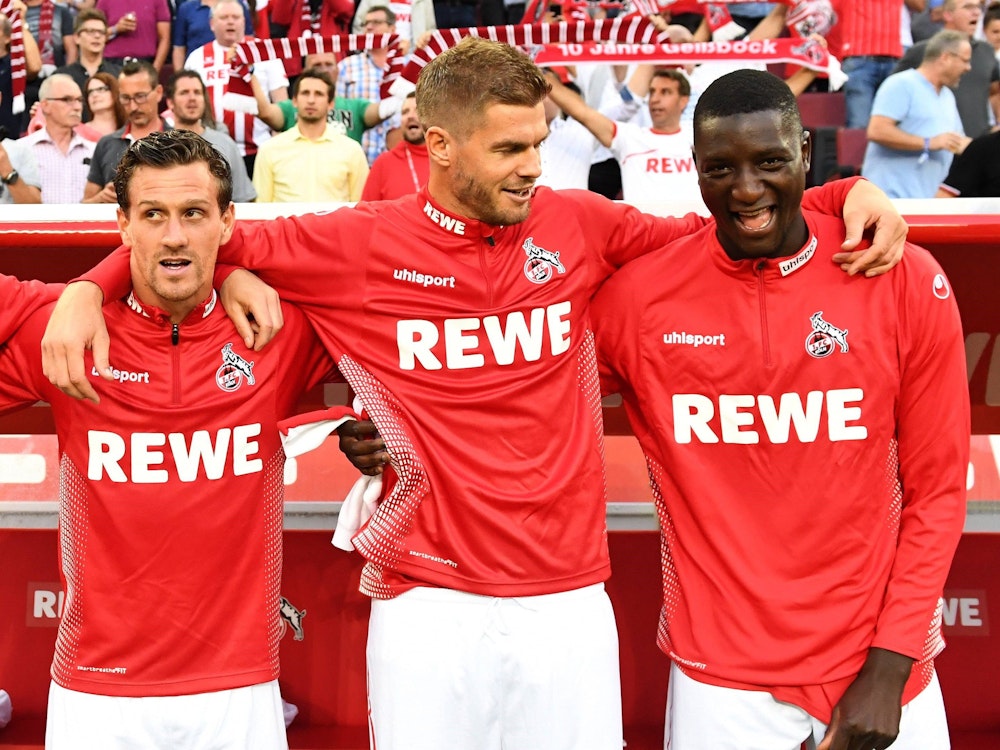 Simon Zoller, Simon Terodde und Serhou Guirassy vom 1. FC Köln stehen nebeneinander vor der Bank und legen die Arme umeinander.