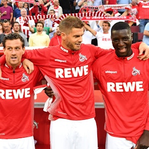 Simon Zoller, Simon Terodde und Serhou Guirassy vom 1. FC Köln stehen nebeneinander vor der Bank und legen die Arme umeinander.