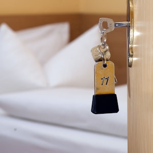 Ein Zimmerschlüssel hängt in einem Gästehaus vor einem Bett im Türschloss.