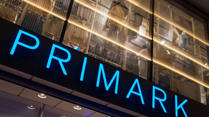 Das Logo des Bekleidungsgeschäfts Primark leuchtet am Abend an der Fassade.