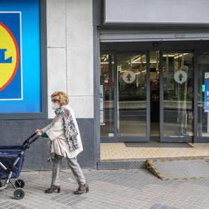 Eine Frau mit Rollator trägt einen Mund-Nasen-Schutz und passiert ein Einkaufsladen von Lidl.