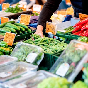 Ein Verkäufer greift an einem Obst- und Gemüsestand auf dem Wochenmarkt in Oldenburg im August 2022 in eine Kiste mit Erbsen.