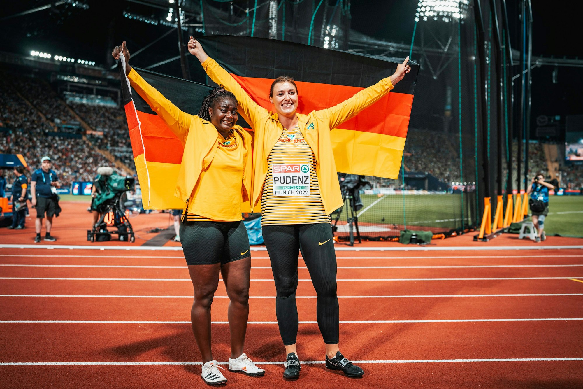 Kristin Pudenz und Claudine Vita halten beide eine Deutschland-Flagge hoch.