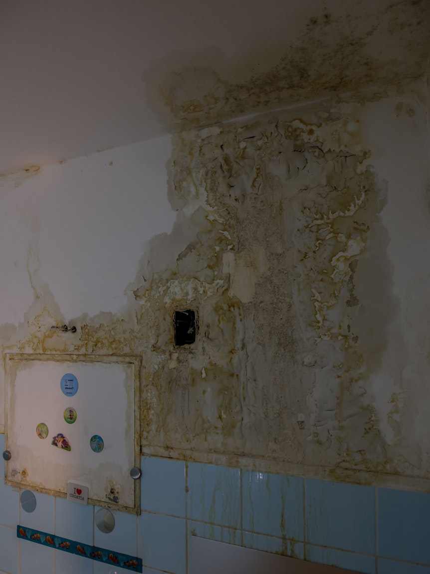 Eine Wand eines Badezimmers ist von Schimmel befallen.