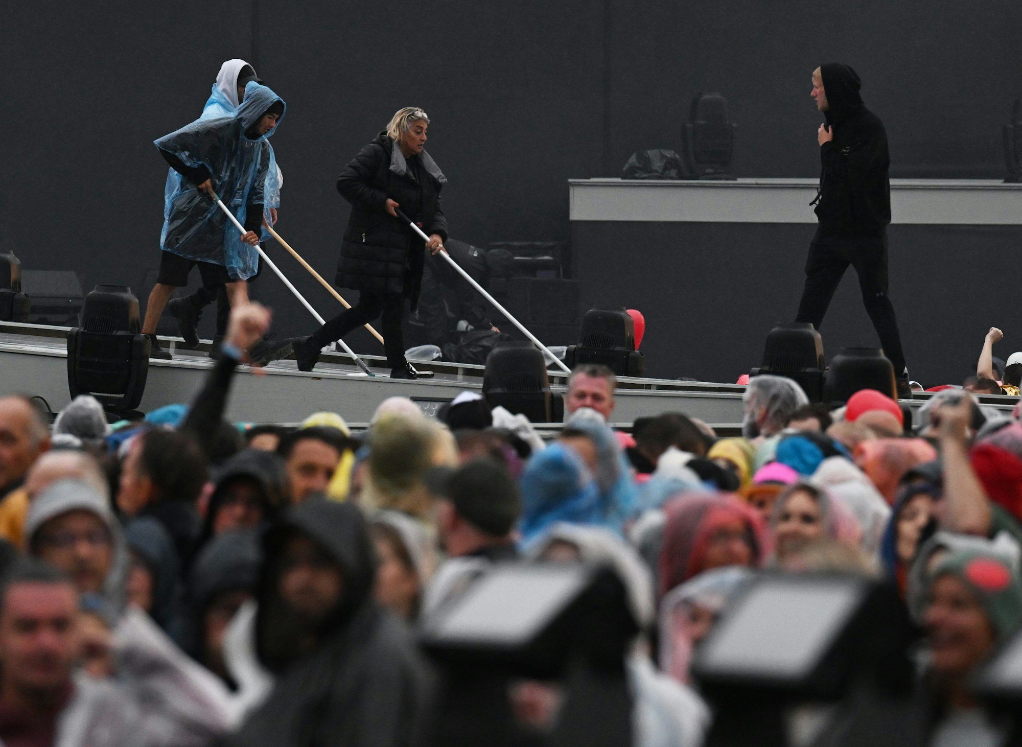 Helfer wischen das Regenwasser vor Beginn des Open-Air-Konzerts von Helene Fischer in der Messe München von der Bühne.