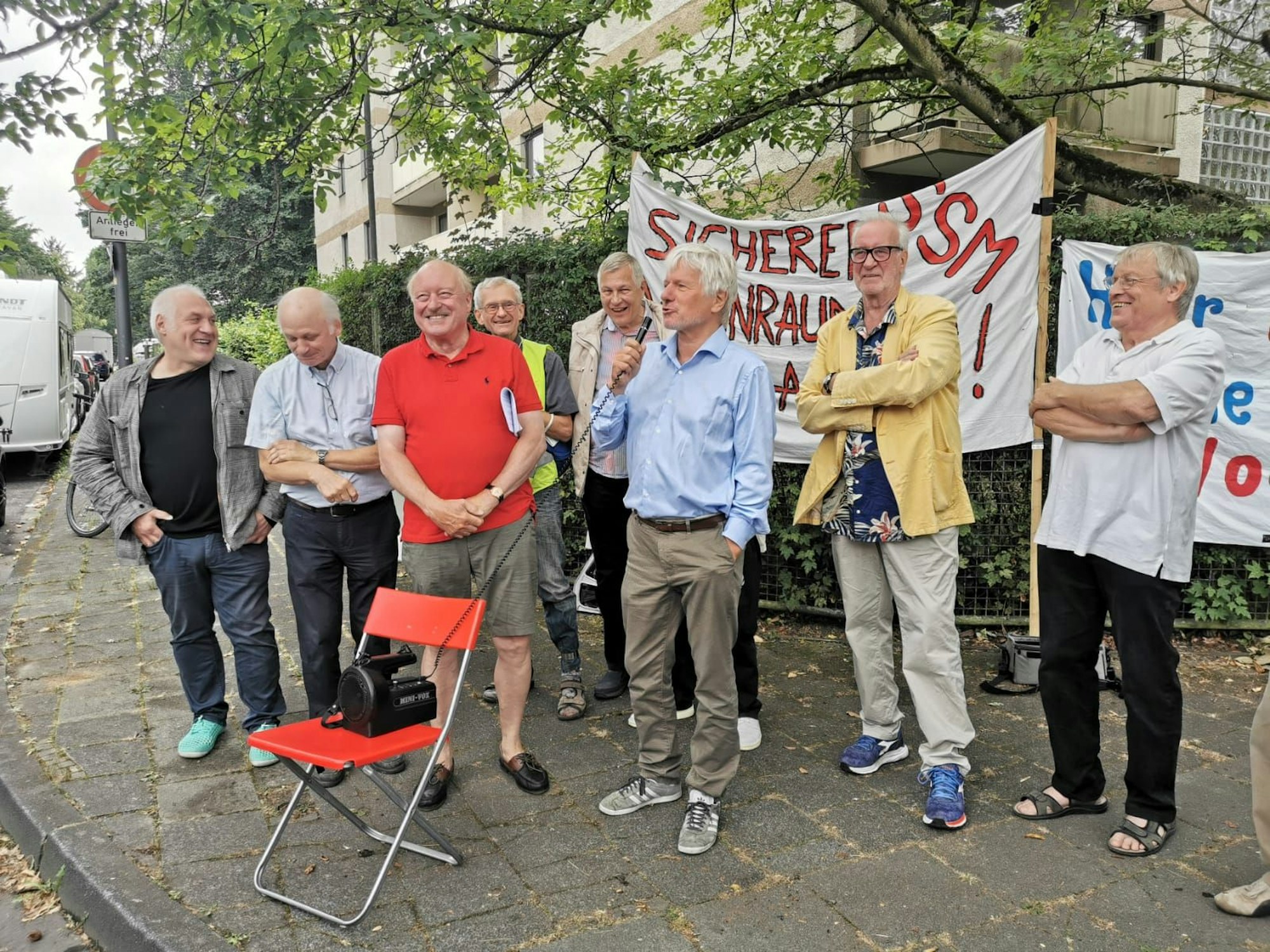 Eine Gruppe Männer steht bei einer Demo an einem Straßenrand.