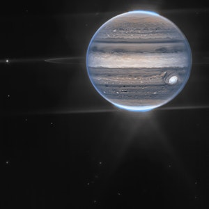 In einer Weitwinkelansicht sieht das James-Webb-Teleskop Jupiter mit seinen schwachen Ringen, die millionenfach schwächer sind als der Planet, und zwei winzige Monde namens Amalthea (der helle Stern links) und Adrastea (rechts daneben, schwach leuchtend auf einem der Ringe). Die blauen Flecken an den Polkappen des Planeten sind Polarlichter.
