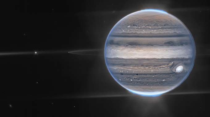 In einer Weitwinkelansicht sieht das James-Webb-Teleskop Jupiter mit seinen schwachen Ringen, die millionenfach schwächer sind als der Planet, und zwei winzige Monde namens Amalthea (der helle Stern links) und Adrastea (rechts daneben, schwach leuchtend auf einem der Ringe). Die blauen Flecken an den Polkappen des Planeten sind Polarlichter.