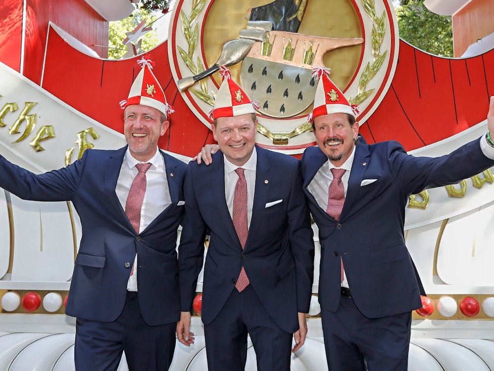 Prinz, Bauer und Jungfrau des neuen Kölner Dreigestirns stehen vor einem Wagen der Roten Funken.