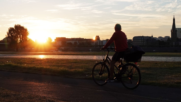 Ein Radfahrer bei Sonnenaufgang am Rheinufer in Düsseldorf. Symbolbild.