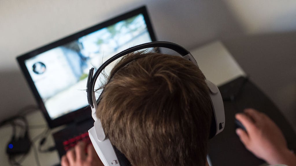 Ein junger Mann sitzt mit einem Headset vor einem Laptop und spielt ein Computerspiel.