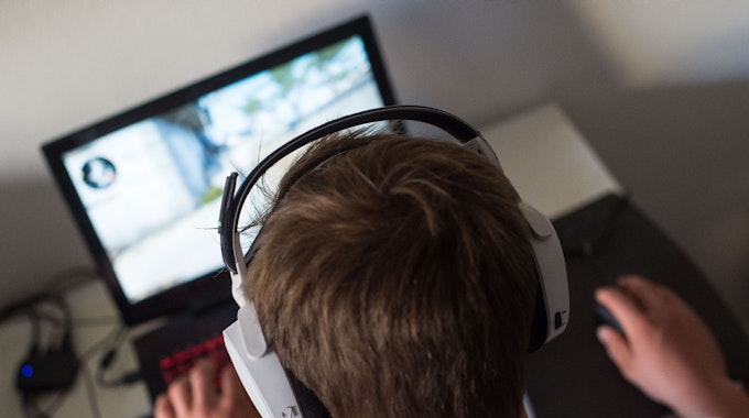 Ein junger Mann sitzt mit einem Headset vor einem Laptop und spielt ein Computerspiel.