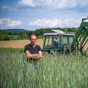 Ulf Allhoff-Cramer, Landwirt, steht in einem Roggen-Feld vor seinem Traktor.