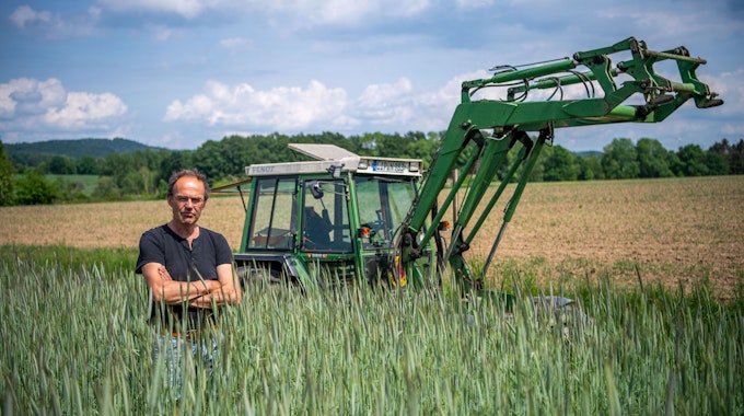 Ulf Allhoff-Cramer, Landwirt, steht in einem Roggen-Feld vor seinem Traktor.