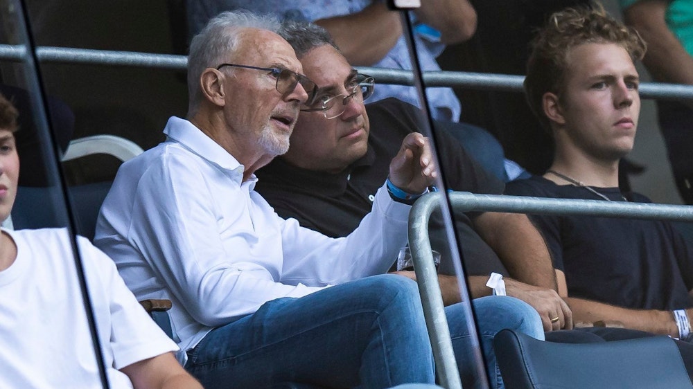 Franz Beckenbauer spricht beim Bundesliga-Spiel der TSG Hoffenheim auf der Tribüne mit seinem Nebenmann