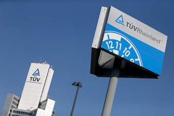 Ein Hinweisschild einer Kfz-Prüfstelle des TÜV Rheinland steht neben der Unternehmenszentrale.