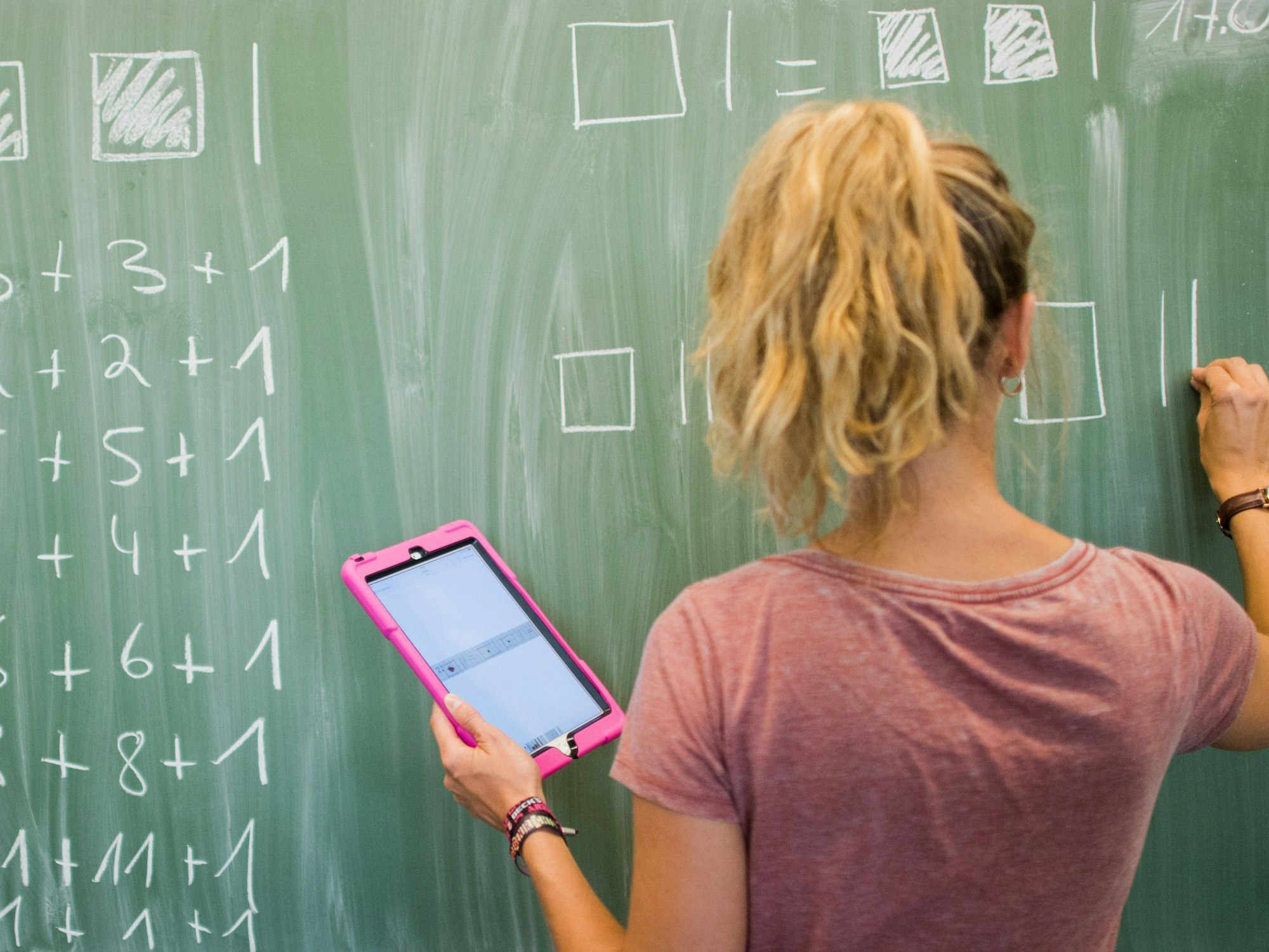 Eine Lehrerin aus Hannover schreibt an eine Schultafel im Mathematikunterricht einer 8. Klasse und blickt dabei auf einen Tablet-Computer iPad.