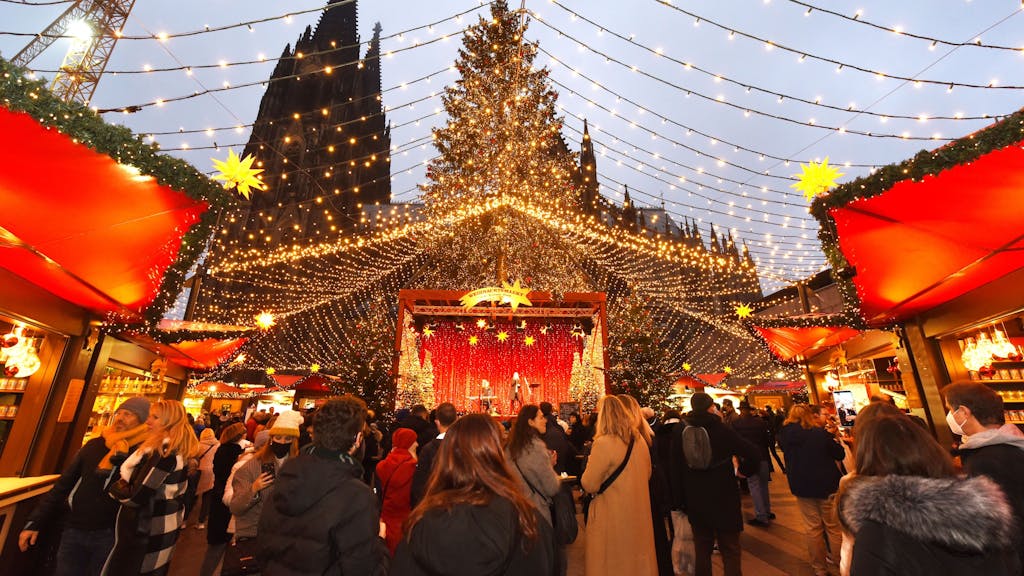 Auf dem Weihnachtsmarkt am Kölner Dom flanieren Besucherinnen und Besucher unter einem „Himmel“ aus Lichterketten.&nbsp;