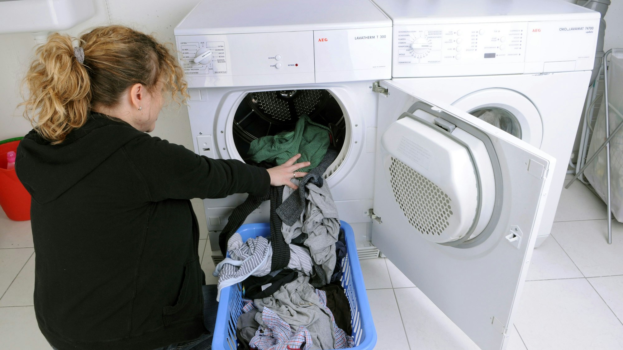 Eine Hausfrau befüllt einen Wäschetrockner mit frisch gewaschener Kleidung.